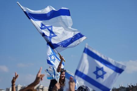 イスラエルの国旗を持つ人たち=13日、イスラエル・テルアビブ近郊(AP=共同)