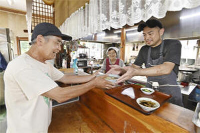 テル子さん（中央）、拓哉さん（右）と一緒に作った注文の定食や丼物をカウンターで受け取る義喜さん（永山能久撮影）