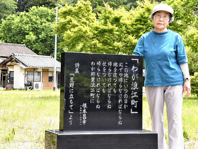 自宅前に建てた歌碑に手を添え、「帰りたかった思いを残してあげたい」と話す洋子さん
