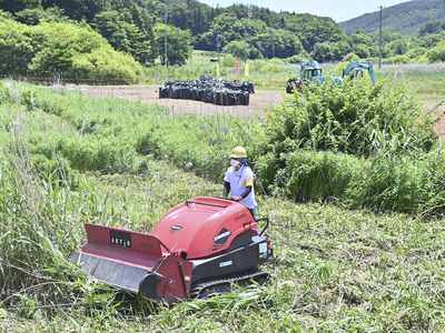 特定帰還居住区域で行われた農地の除草作業。後方は表土を削り取るなどの除染工事＝２０２４年６月２０日、浪江町羽附地区
