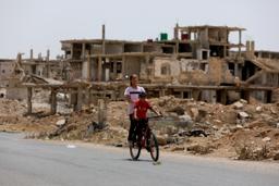 　破壊された家の前を自転車に乗って通り過ぎる子ども＝１７日、シリア南部ダルアー県（ゲッティ＝共同）