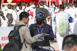 　中国の全国一斉大学入試「高考」の会場前で所持品をチェックされる受験生（左）＝７日、北京（共同）