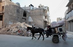 　シリア北部アレッポで、破壊された建物のそばを通る家財道具を積んだ馬車＝６月２４日（ロイター＝共同）