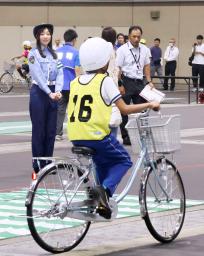 　自転車の乗り方などを競う大会で、実技テスト中の参加者（手前）を見守る愛知県警交通安全大使の須田亜香里さん（奥左）＝２９日午前、名古屋市