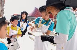 　屋外で働くスタッフらにスポーツドリンクをついで回る仕事体験の小学生ら＝３日午後、大阪市此花区の夢洲