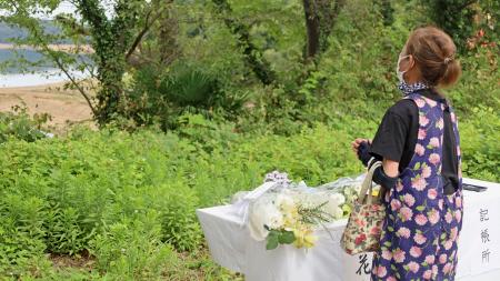 　愛知県犬山市の「入鹿池」のそばで献花し、手を合わせる女性＝１４日午前