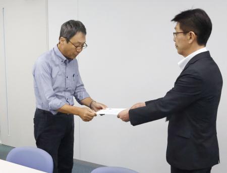 　米軍と日本政府に抗議を求める文書を手渡す地元市民団体の久米慶典共同代表（左）＝１８日午前、山口県岩国市役所
