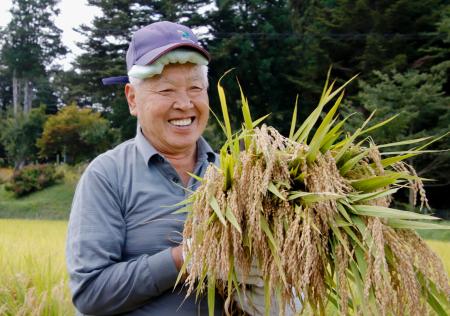 　福島県飯舘村長泥地区で稲を刈り、笑顔を見せる庄司喜一さん＝２４日午前