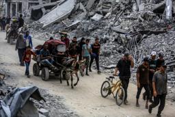 　停戦合意発効を受け、自宅に戻るため破壊された建物の間を移動するパレスチナ人ら＝１２日、ガザ南部ハンユニス（ゲッティ＝共同）